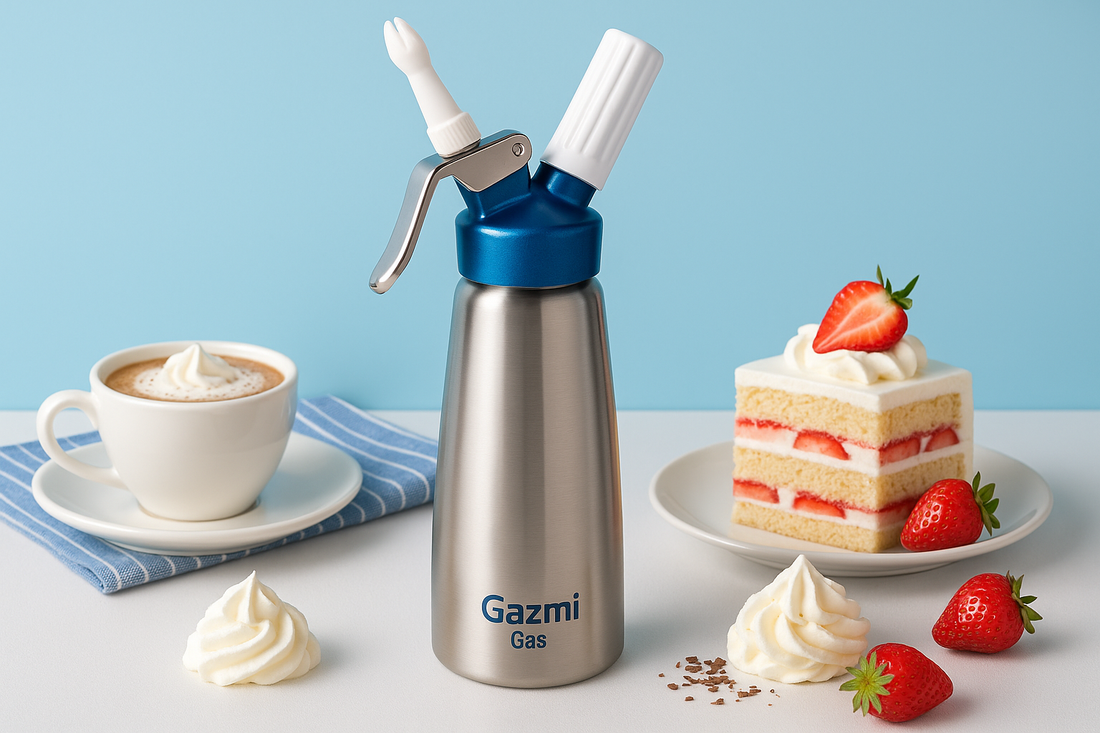 A sleek stainless steel whipped cream dispenser branded with Gazmi Gas, placed on a white table with a cup of cappuccino topped with whipped cream and a slice of strawberry shortcake against a soft blue background.